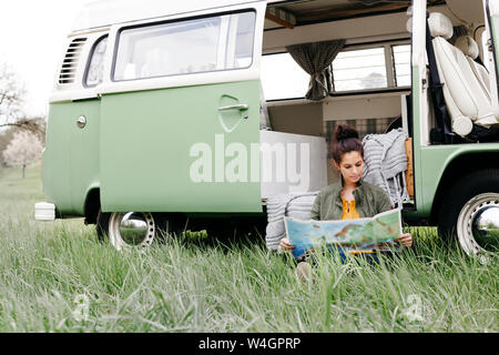 Junge Frau Studium Karte, im Gras sitzen, vor ihr Wohnmobil Stockfoto