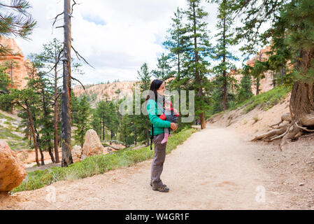 Frau, die ihre Tochter in einem tragesitz bei Hoodoos im Bryce Canyon, Utah, USA Stockfoto