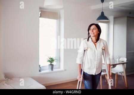 Reife Frau mit Krücken, allein zu Hause Stockfoto