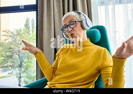 Ältere Frau im Sessel sitzen, Musik hören mit Kopfhörern Stockfoto