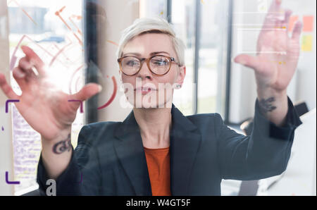 Geschäftsfrau berühren Glaswand mit Daten in Office Stockfoto