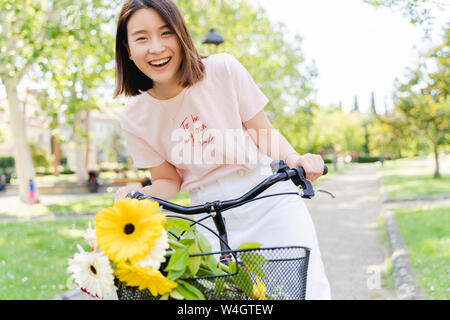 Porträt der glückliche junge Frau mit Blumen und Fahrrad im Park Stockfoto