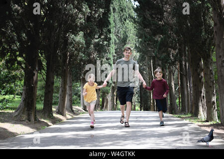 Vater mit zwei Kindern, die in einer kleinen, mit Bäumen gesäumten Straße Stockfoto