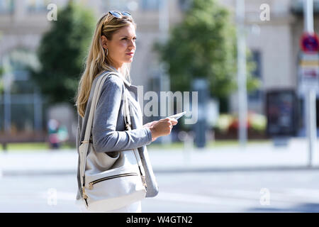 Junge Geschäftsfrau, die die Arbeit mit digitalen Tablet im Stehen mit Koffer auf der Straße Stockfoto