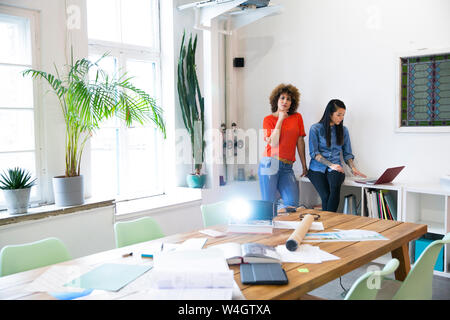 Zwei Frauen im modernen Büro mit Videoprojektor auf Tisch Stockfoto