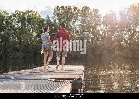 Junges Paar Hand in Hand auf Steg an einem entfernten See Stockfoto