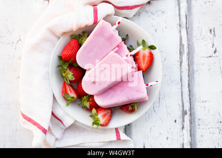 Selbstgemachte Erdbeer Joghurt Eis am Stiel mit frischen Erdbeeren in eine Schüssel auf weißem Holz Stockfoto