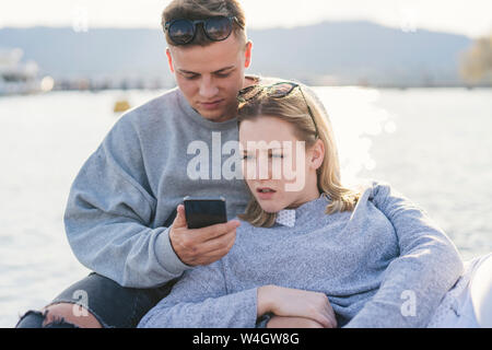 Junges Paar auf Steg am Zürichsee am Handy, Zürich, Schweiz Stockfoto