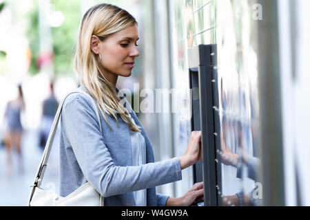 Junge Geschäftsfrau mit einer Kreditkarte Geld auf ein Geldautomat im Freien zu widerrufen Stockfoto