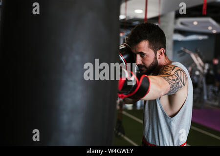 Junger Mann in Boxhandschuhe gegen Boxsack Stockfoto