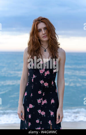 Porträt der jungen Frau Sommer Kleid mit Blumenmuster steht vor dem Meer Stockfoto