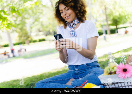 Entspannt Frau mit Handy und Kopfhörer bei einem Picknick im Park Stockfoto