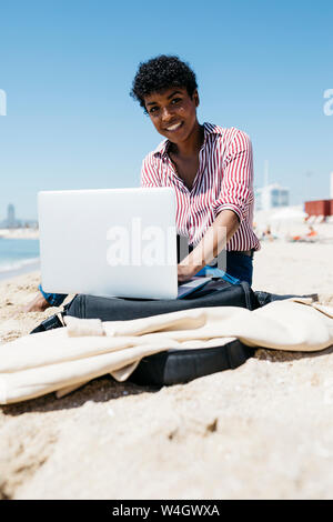 Frau am Strand zu sitzen, während der Arbeit mit dem Laptop Stockfoto