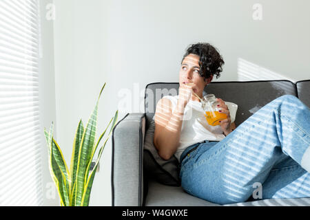 Entspannt junge Frau sitzt auf der Couch mit einem alkoholfreien Getränk Stockfoto