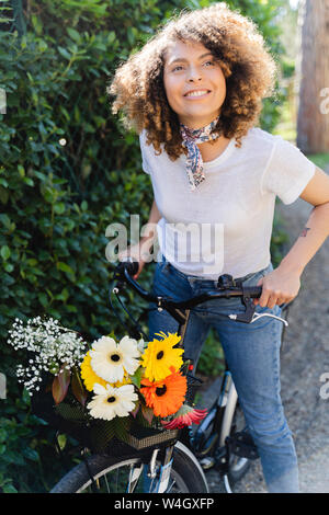 Lächelnde Frau mit Blumen und Fahrrad im Park Stockfoto