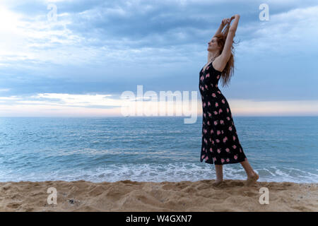 Glückliche junge Frau tanzen am Strand am Abend Stockfoto