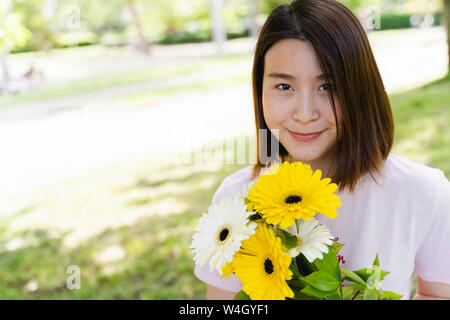 Portrait von lächelnden jungen Frau mit Blumen im Park Stockfoto