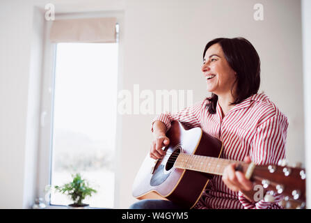 Reife Frau gerne Gitarre spielen zu Hause Stockfoto