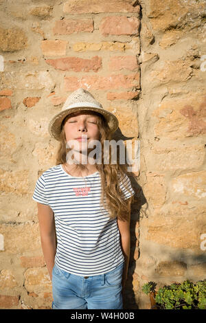 Mädchen mit Strohhut lehnte sich an der Wand mit geschlossenen Augen, Toskana, Italien Stockfoto