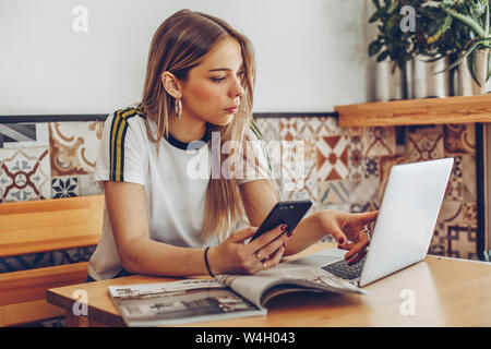 Junge Frau mit Handy und Laptop im Cafe Stockfoto