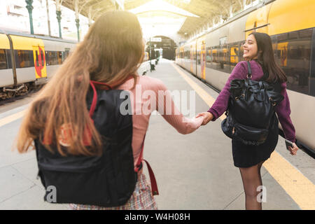 Zurück Blick auf zwei junge Frauen mit Rucksäcken Hand in Hand auf der Plattform, Porto, Portugal Stockfoto