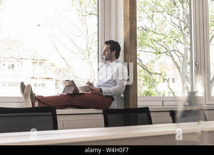 Junge Unternehmer sitzen auf Fensterbank, mit digitalen Tablet Stockfoto