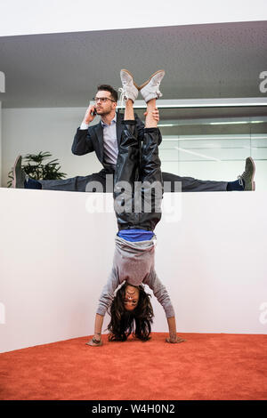 Unternehmer im Amt, die Beine der Frau macht einen Handstand Stockfoto