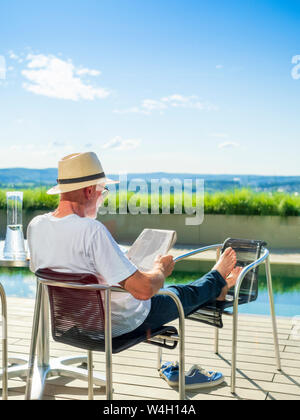 Ansicht der Rückseite des älteren Mann lesen newspapper, Sitzen am Pool Stockfoto