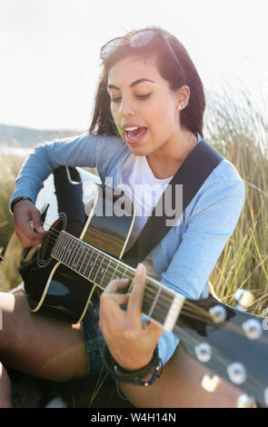 Junge Frau singen und Gitarre spielen am Strand Stockfoto