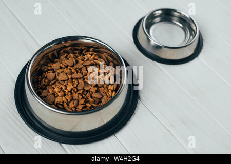 Metallschale mit Tiernahrung und leere Schüssel auf weißem Holz- Oberfläche Stockfoto