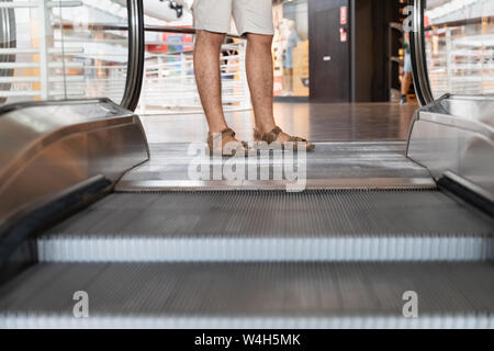 Junge Mann in kurzen Hosen steigt auf einer Rolltreppe in einem Einkaufszentrum. Stockfoto