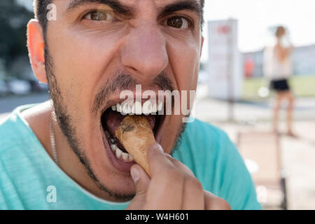 Ein junger Mann ißt schwarze Eis in einem Kegel. Wegen der schwarzen Eis, sein ganzes Gesicht und Zähne sind schwarz. Stockfoto