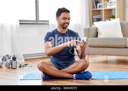 Inder mit Smartphone auf der Trainingsmatte zu Hause Stockfoto