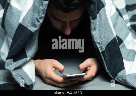 Junge Mann im Schlafanzug mit einem Handy, während im Bett lag. Stockfoto