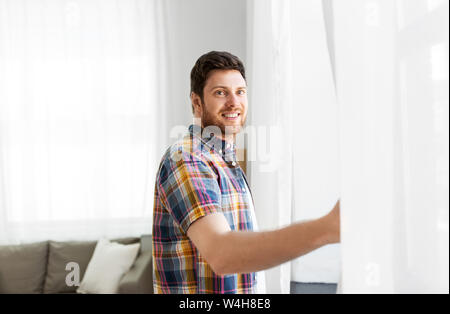 Junger Mann öffnen Fenster Vorhang zu Hause Stockfoto