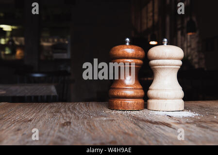 Holz- Salz und Pfeffer Mühle auf einem Holztisch in dunklen Cafe. Kopieren Sie Platz. Salz- und Pfefferstreuer. Vintage Style. Gewürzen bestreut. Stockfoto