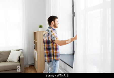 Junger Mann öffnen Fenster Vorhang zu Hause Stockfoto