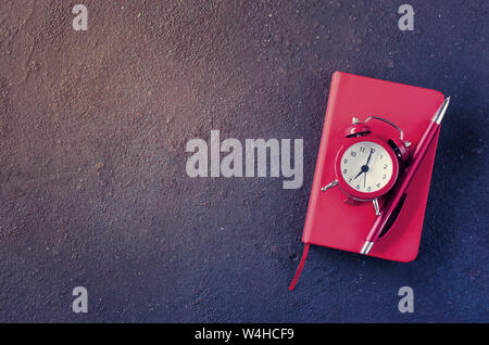 Wecker, Notizblock und Stift auf dunklem Hintergrund. Konzept Zeitmanagement oder Bildung. Kopieren Sie Platz. Stockfoto