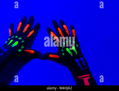 Nahaufnahme von Neon bemalte Hand gegen den blauen Wand. Stockfoto