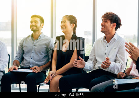 Gruppe von Multiethnischen Kollegen lächelnd und applaudierten beim Sitzen in der Nähe der Fenster während Business Seminar im Büro Stockfoto