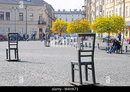 Stühle im Ghetto Heldenplatz Monument mit dem apteka Pod Orlem Pharmacy Museum hinter sich. Stockfoto