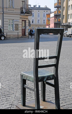 Einzelne große Stuhl, (representng 1000 nach Todesfällen) im Ghetto Heldenplatz Denkmal, mit Apteka Pod Orlem Pharmnacy Museum hinter sich. Stockfoto