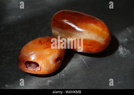 Trommelsteine karneol Steine auf grauem Schiefer Hintergrund, beleuchtet von der Sonne Stockfoto