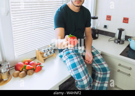 Ein junger Mann sitzt in der Küche und hält reife Erdbeeren in den Händen. Steam bietet die Beeren zu versuchen. Stockfoto