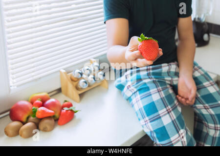 Ein junger Mann sitzt in der Küche und hält reife Erdbeeren in den Händen. Steam bietet die Beeren zu versuchen. Stockfoto