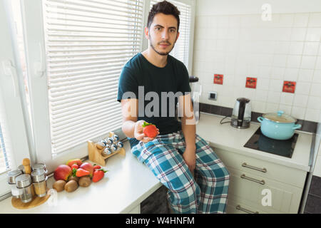Ein junger Mann sitzt in der Küche und hält reife Erdbeeren in den Händen. Steam bietet die Beeren zu versuchen. Stockfoto