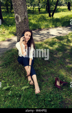 Business woman ruhend Sitzen unter den Baum ohne Schuhe und Telefonieren in einem öffentlichen Park selektiven Fokus Stockfoto
