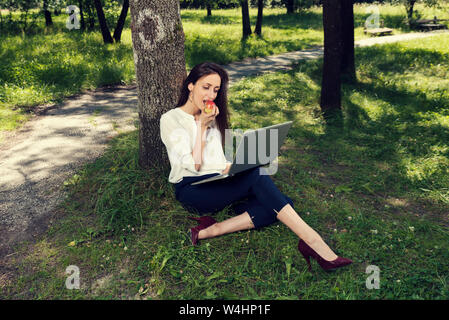 Business woman unter dem Baum apple Essen und Arbeiten auf Ihrem Laptop selektiven Fokus sitzen Stockfoto