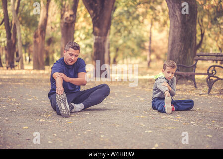 Kleinen Jungen und seinem Vater tun stretching Übung zusammen in den Park. Vater und Sohn verbringen Zeit miteinander und einen gesunden Lebensstil führen. Arbeiten Stockfoto