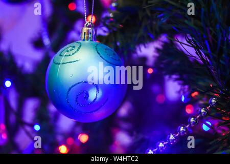Blaues Weihnachtsschmuck hängt im Dezember an einem Weihnachtsbaum in einem Familienhaus, mit anderen Dekorationen und unscharfen Lichtern im Hintergrund. Stockfoto